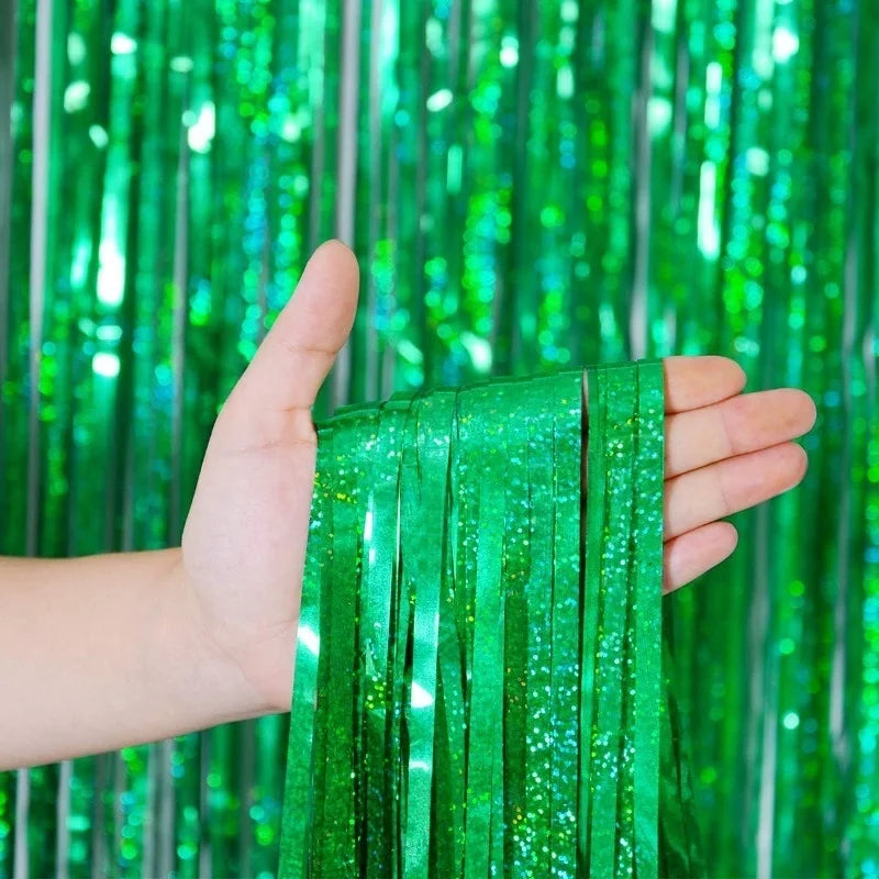 A hand holds a vertical set of metallic green foil tinsel fringe used as a backdrop.