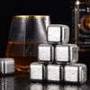 A stack of clear, textured stainless steel ice cubes resting on a dark surface next to an amber drink and a bottle.