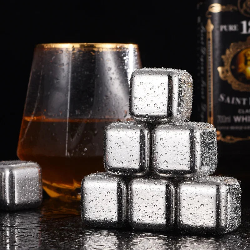 A stack of clear, textured stainless steel ice cubes resting on a dark surface next to an amber drink and a bottle.
