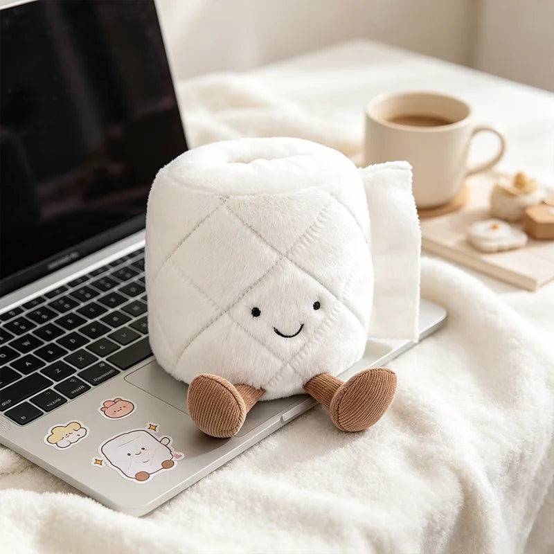 A white plush toy shaped like a toilet paper poop plunger with a smiling face resting on a laptop.