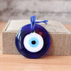 A dark blue glass evil eye amulet pendant with a blue string on a light brown box.