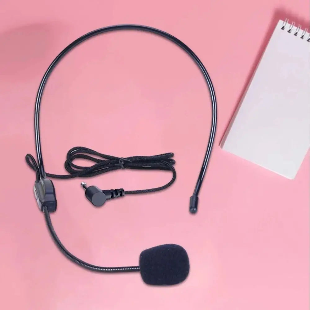 A black wired headset microphone with an adjustable boom and a foam windscreen is shown against a pink background.