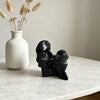 A black resin sculpture depicting an abstract kissing couple resting on a white marble surface.
