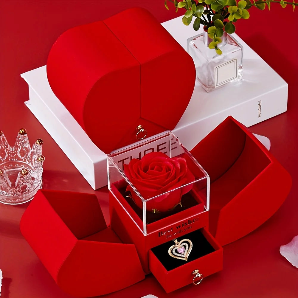 A red heart-shaped gift box containing a pink rose and a gold pendant necklace on a white display box.