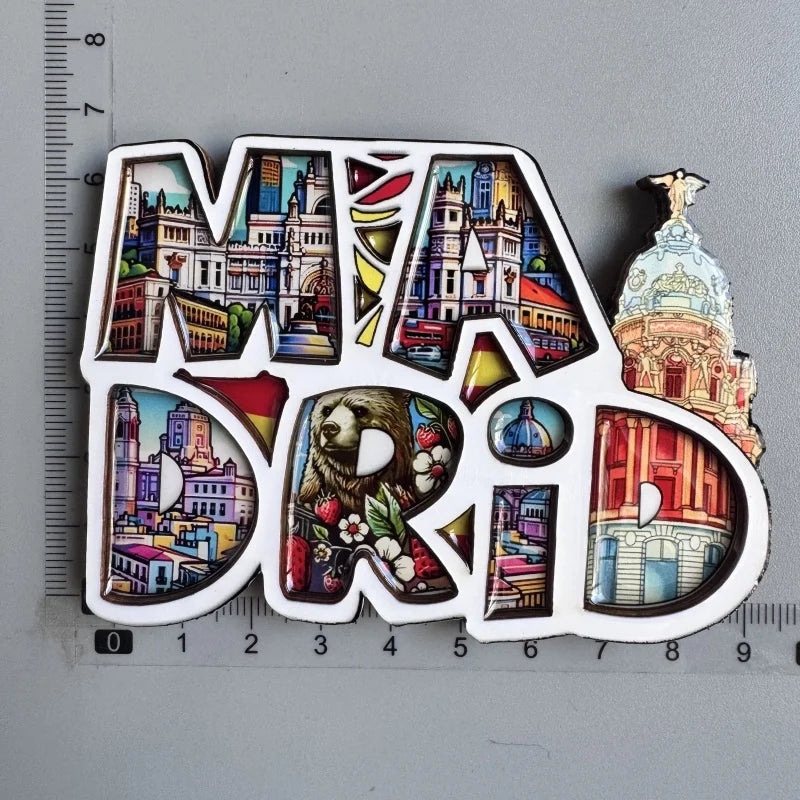 A collection of wooden destination fridge magnets shaped like the letters M A D, featuring colorful cityscapes and landmarks.