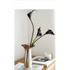 A silver-plated ceramic vase holds a single dark purple orchid with long stem against a white background.