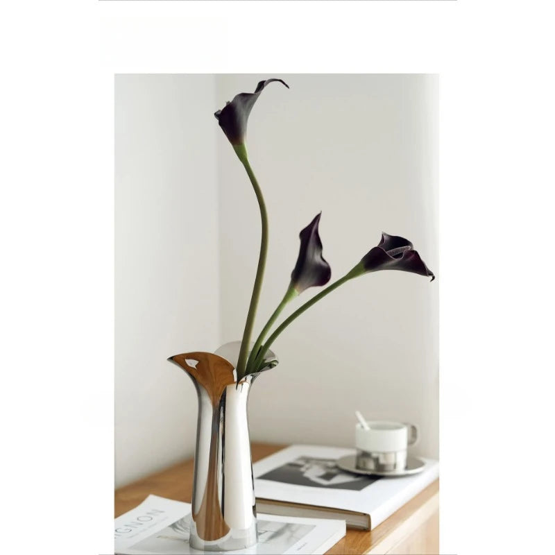 A silver-plated ceramic vase holds a single dark purple orchid with long stem against a white background.