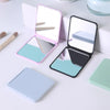 A pink and silver compact foldable travel makeup mirror with a magnifying surface is shown next to its closed case.
