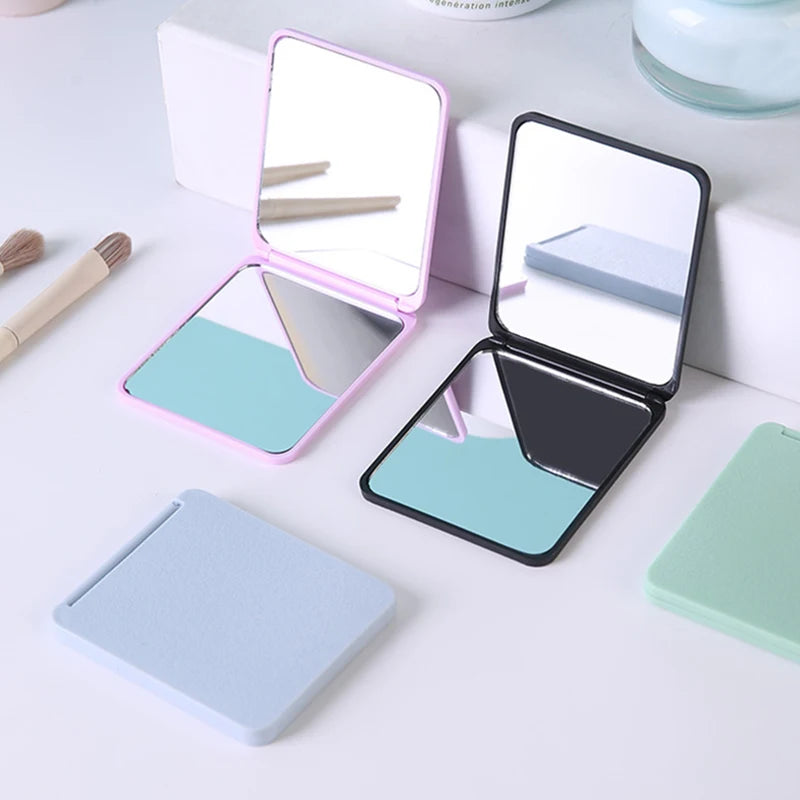 A pink and silver compact foldable travel makeup mirror with a magnifying surface is shown next to its closed case.