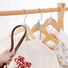A hand is hanging a light-colored t-shirt on a wooden hanger with a metal hook connector.