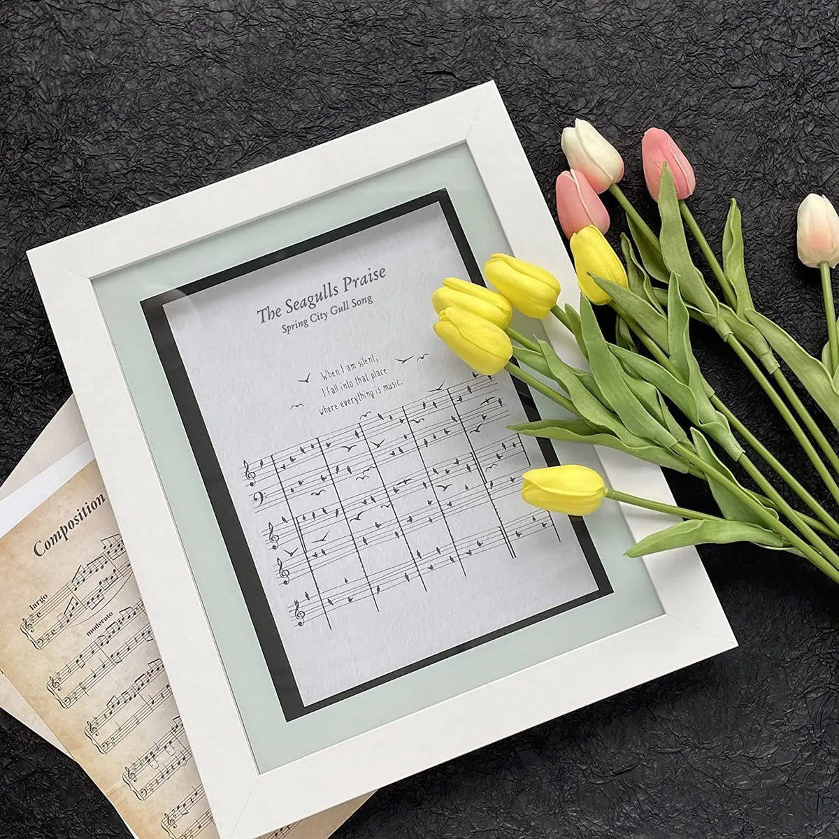 A framed sheet music display featuring the song The Seagulls Praise, surrounded by fresh tulips.