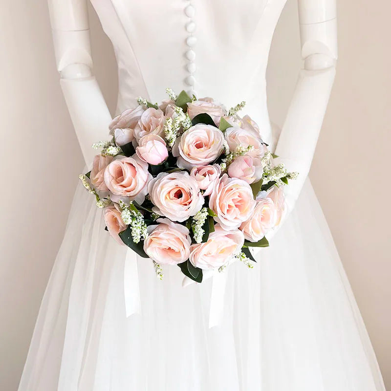 A bridal bouquet of soft pink and blush roses with white accents held by a model in a white dress.