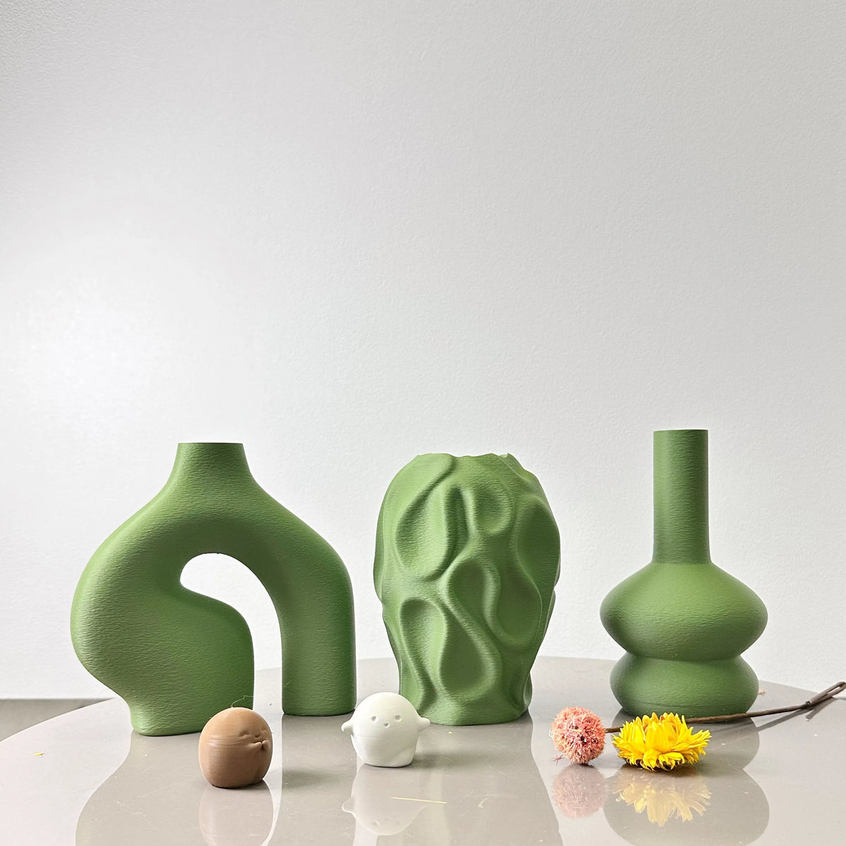 A set of three organic, textured green geometric vases displayed on a white surface.