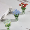 A glass flower bouquet featuring red and blue blossoms displayed in clear glass vases on a white marble surface.