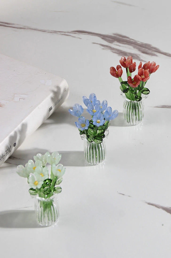 A glass flower bouquet featuring red and blue blossoms displayed in clear glass vases on a white marble surface.