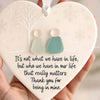A heart-shaped sea glass Christmas ornament with a white background and a light blue pendant is held in a hand.