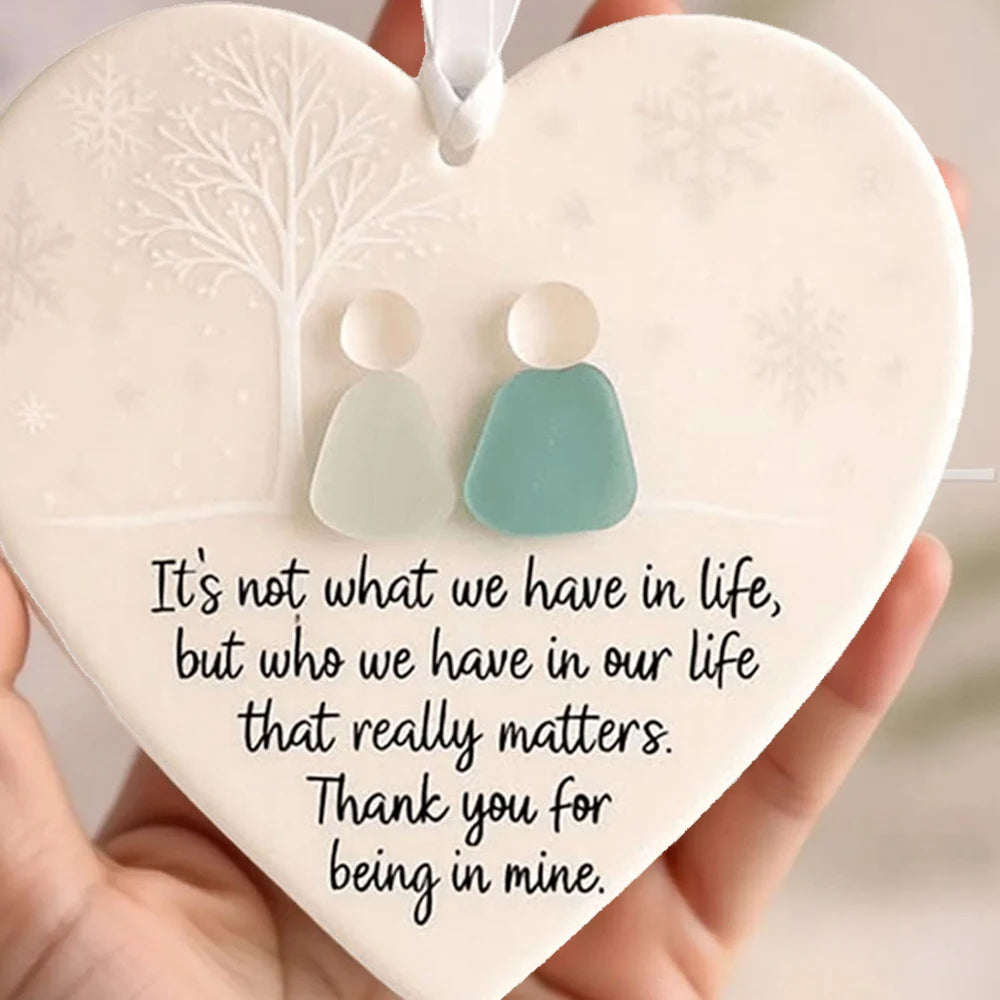 A heart-shaped sea glass Christmas ornament with a white background and a light blue pendant is held in a hand.