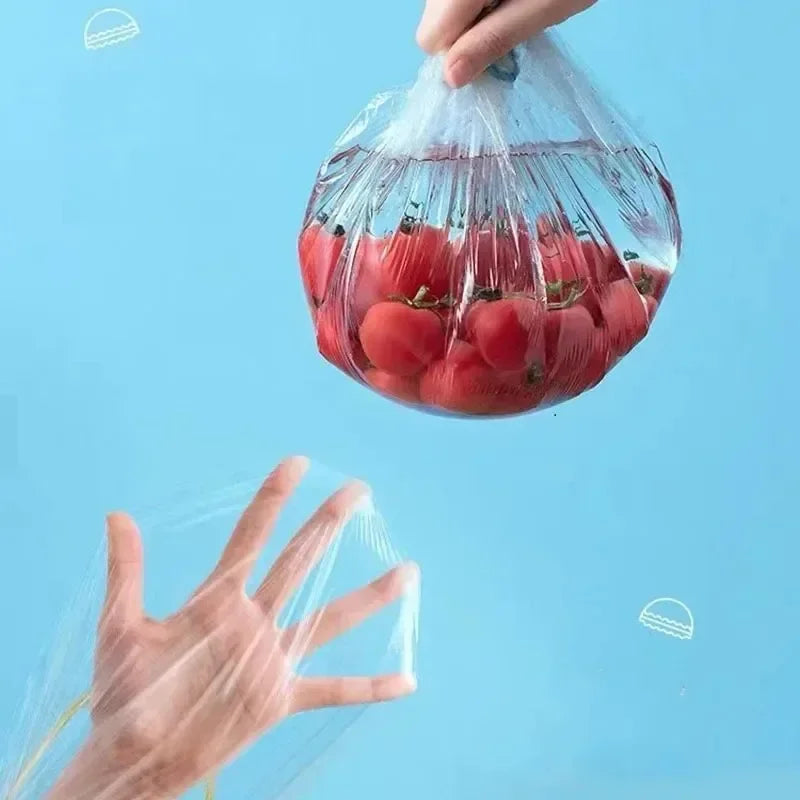 A hand is lifting a clear elastic food cover filled with red tomatoes.