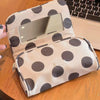 A beige canvas travel makeup bag with dark polka dots and a rectangular mirror resting on a wooden surface.