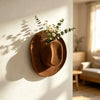 A terracotta wall vase holder with a felt hat design and yellow wildflowers casting a shadow on a white wall.