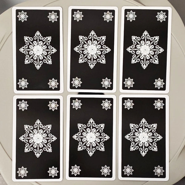 A set of black tarot cards featuring white snowflake designs arranged in a circular pattern.