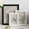 A collection of framed floral still life paintings featuring pink and white flowers in glass vases displayed on a white surfa
