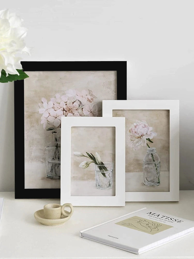 A collection of framed floral still life paintings featuring pink and white flowers in glass vases displayed on a white surfa