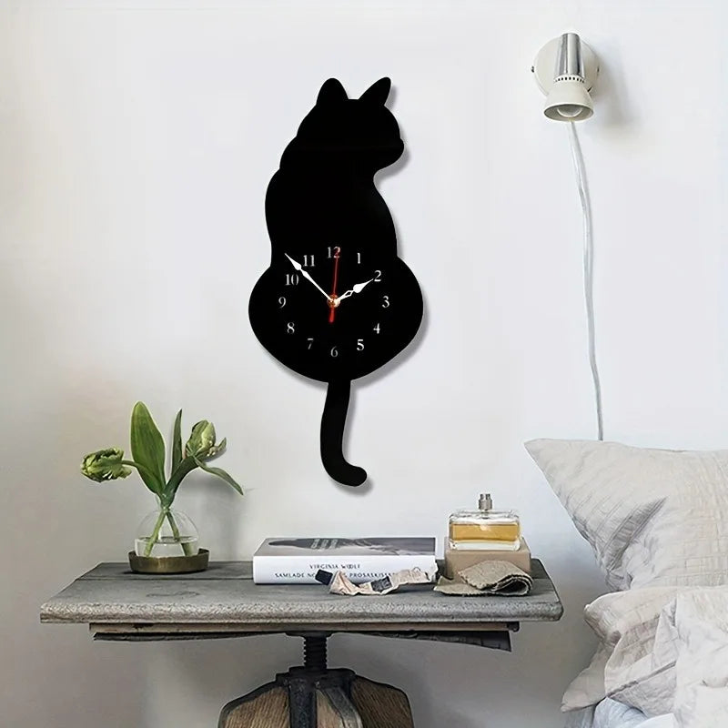 A black cat pendulum wall clock with a moving tail is displayed on a wooden table.