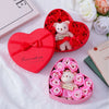 A pink heart-shaped gift box filled with red roses and a small white teddy bear.