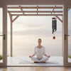 Une personne est assise en posture de méditation sur un plancher en bois, regardant la mer à travers une grande porte vitrée.