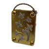 A small gold-colored metal box with a wire loop, featuring pressed dried flowers.