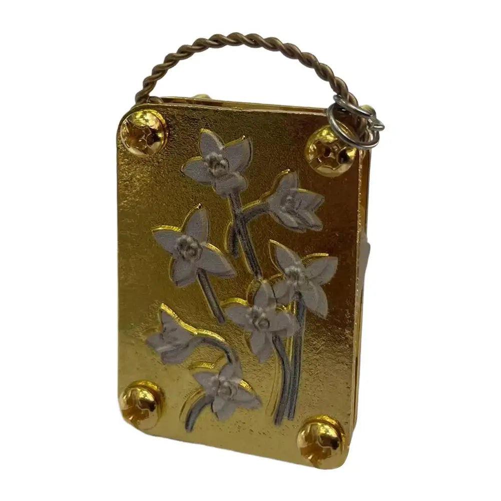 A small gold-colored metal box with a wire loop, featuring pressed dried flowers.