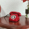 A small red retro rotary desk phone miniature placed on a wooden surface.