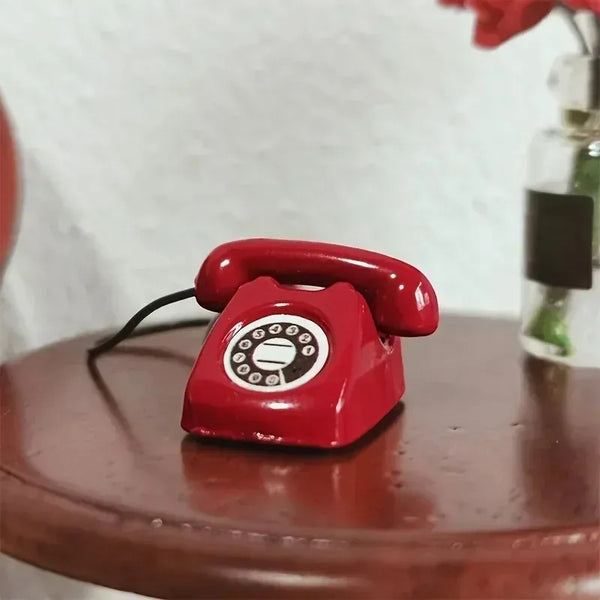 A small red retro rotary desk phone miniature placed on a wooden surface.
