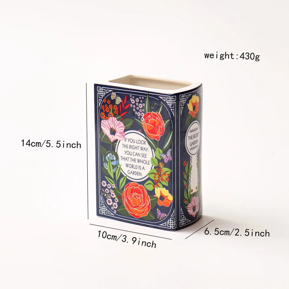 A ceramic book-shaped vase with a vintage finish featuring floral patterns and text on the side.