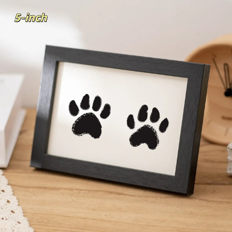 A black wooden photo frame displaying two black paw prints on a light background.