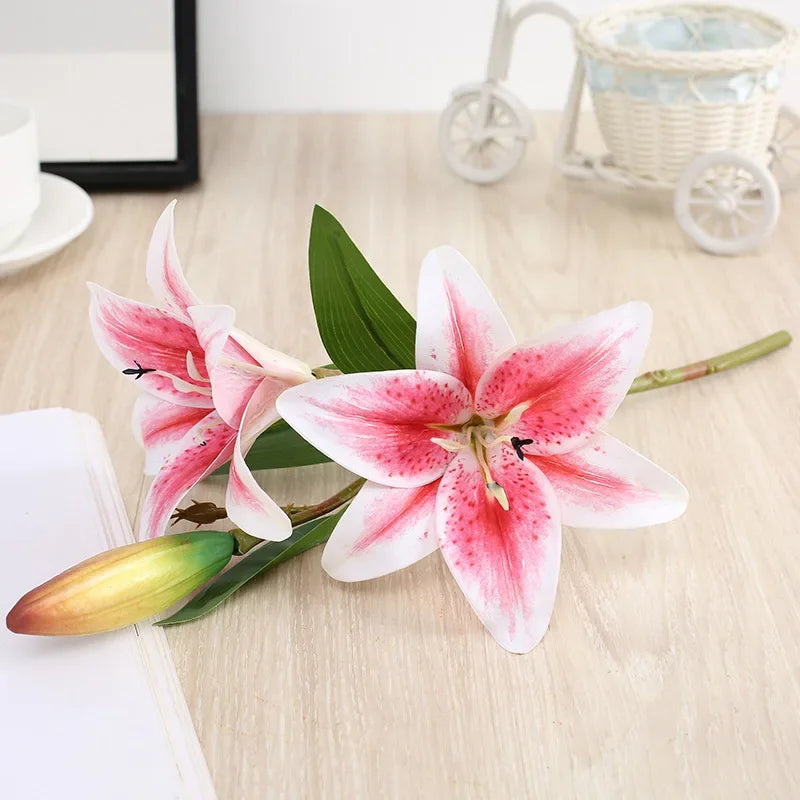 Realistic silk lily flower stem with three pink and white blooms on a green leaf.