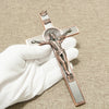 A hand holds a bronze crucifix with a St. Benedict medal and INRI plaque on a neutral background.