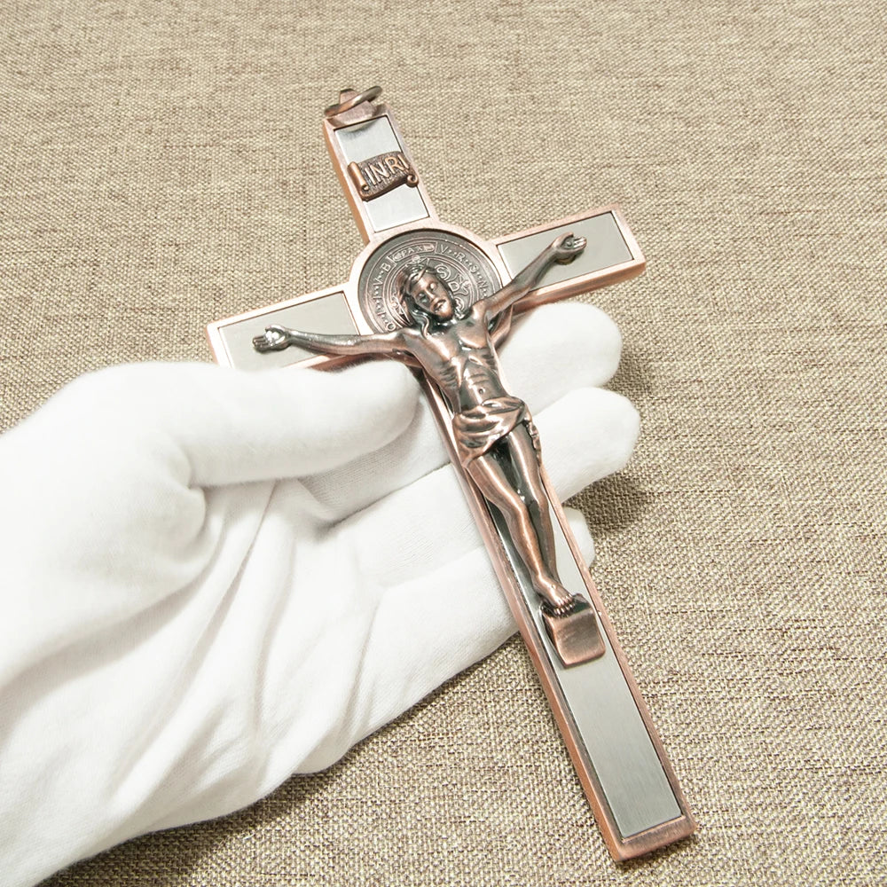 A hand holds a bronze crucifix with a St. Benedict medal and INRI plaque on a neutral background.