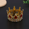 A golden crown made of gold-toned metal and red jewels, used as a cake topper or hair accessory.