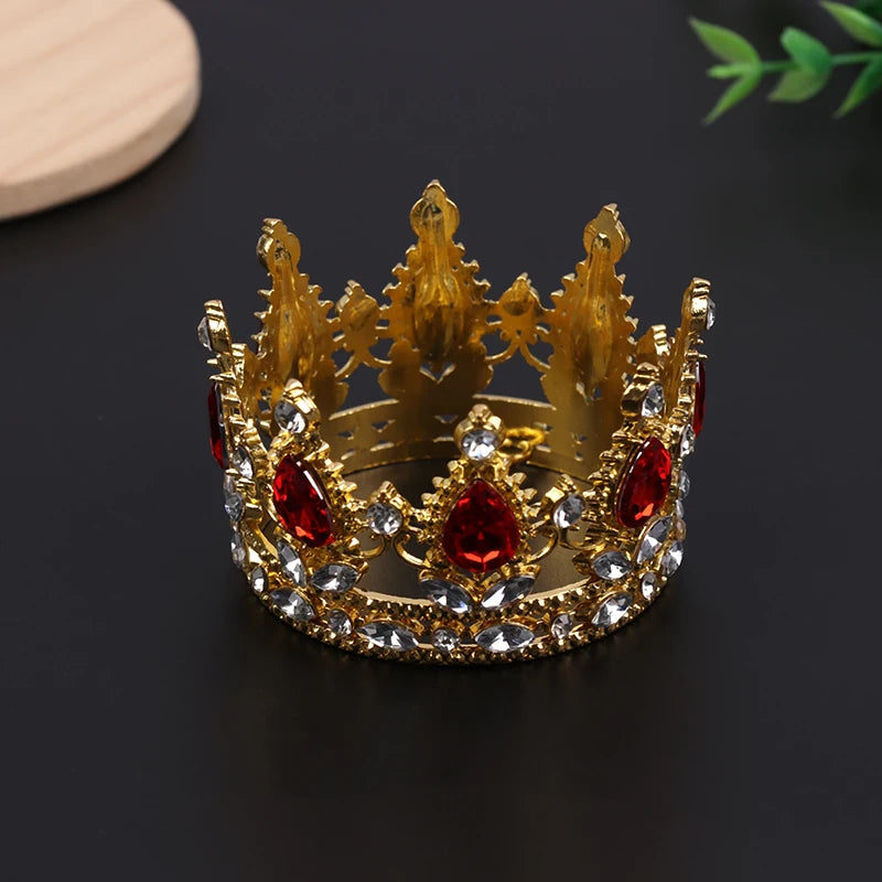 A golden crown made of gold-toned metal and red jewels, used as a cake topper or hair accessory.