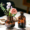 A dark amber glass vase filled with pink and white flowers sits on a white surface.