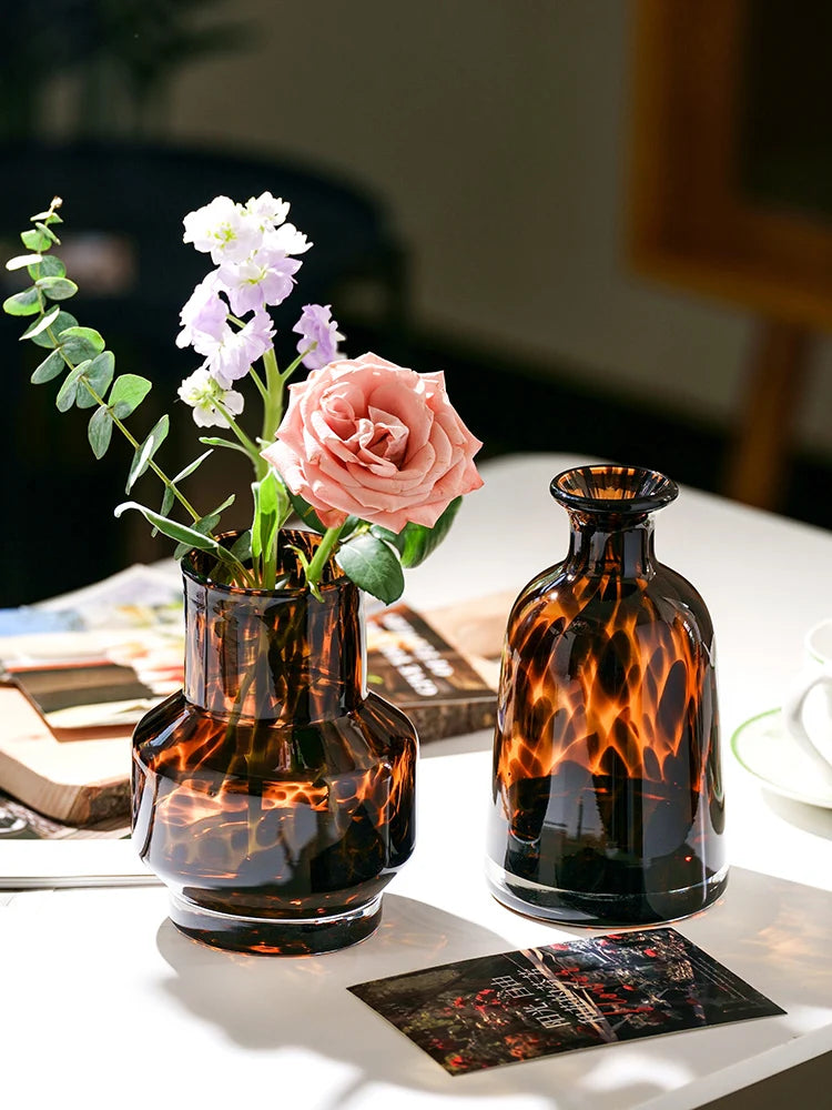 A dark amber glass vase filled with pink and white flowers sits on a white surface.