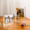 A clear acrylic magnetic photo frame displaying a portrait of a person and a dog surrounded by dried flowers.