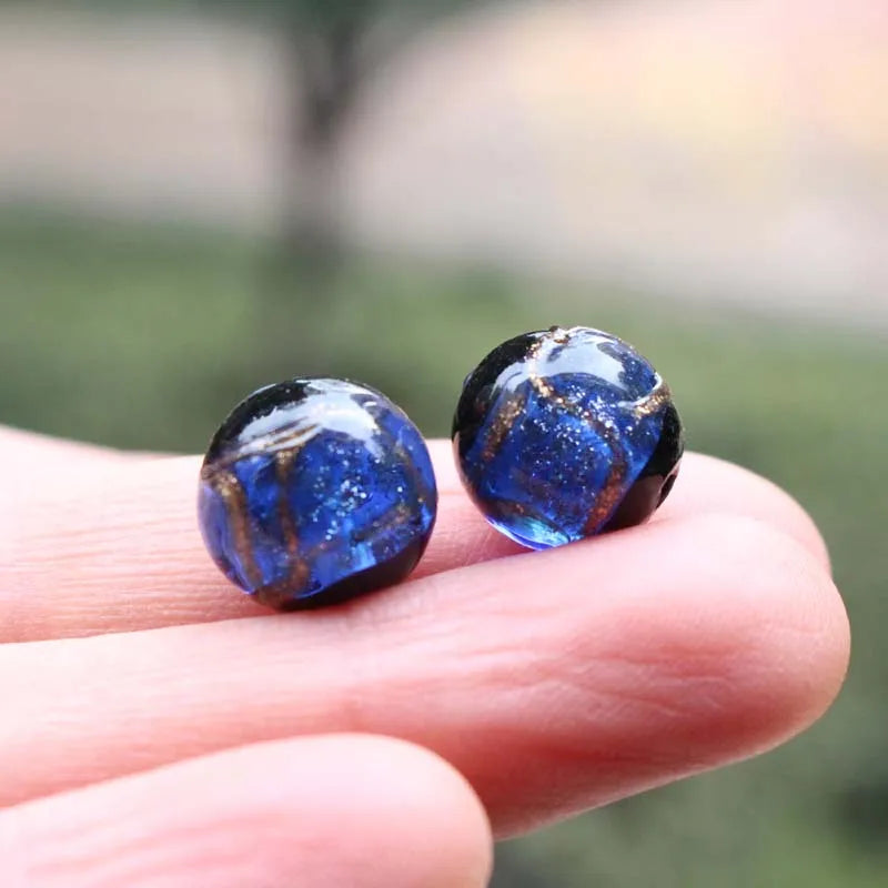 Two polished blue glass beads with gold accents resting on a person's finger.