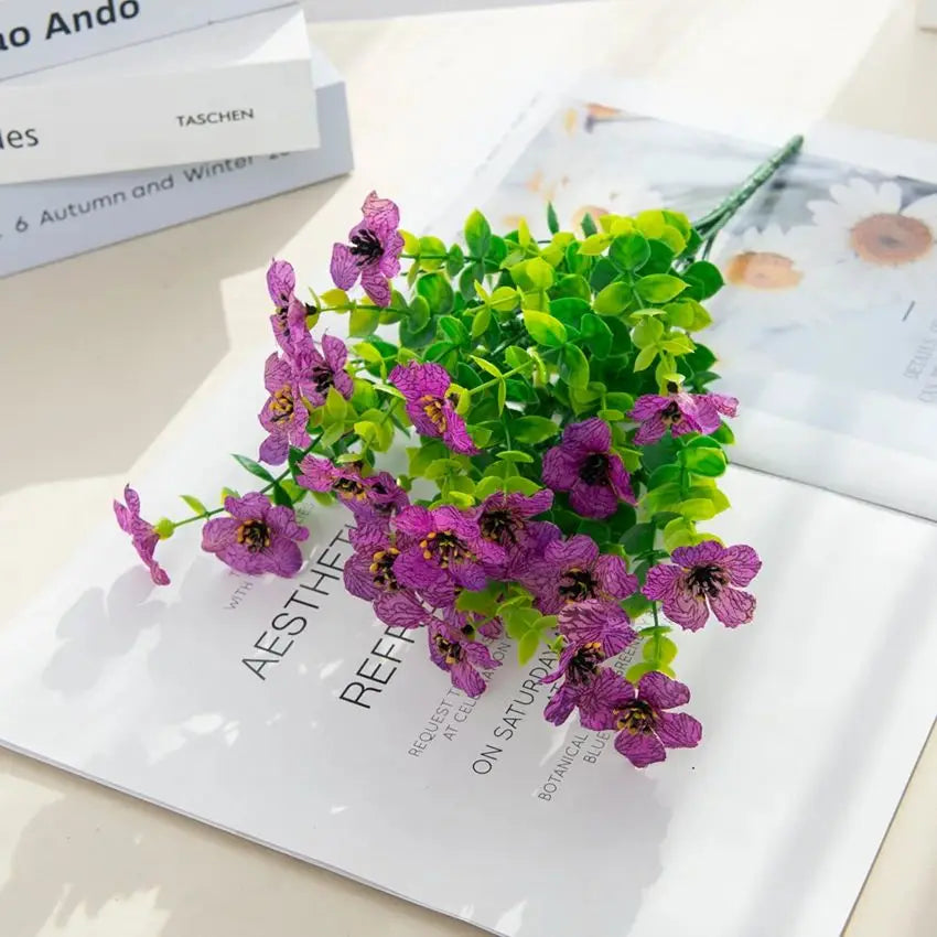 A bouquet of purple and pink silk eucalyptus and violet artificial flowers on a white background.