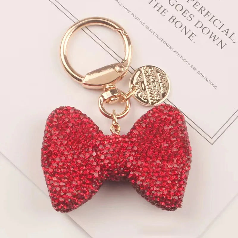 A red sparkling rhinestone bow keychain with a gold split ring and charm.