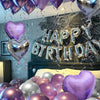 A display of purple and silver metallic balloons, including heart-shaped balloons, decorating a wall for a birthday celebrati