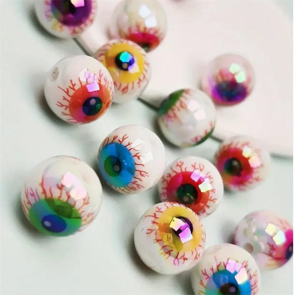 A set of ten iridescent acrylic eyeball spacer beads with colorful, detailed designs scattered on a white surface.