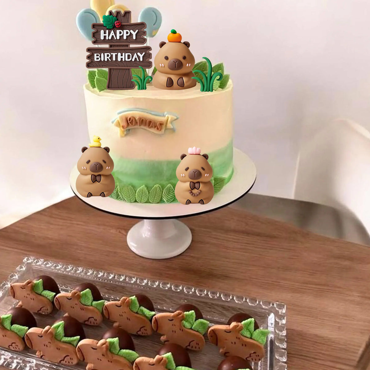 A tiered birthday cake decorated with capybara animal figures and green foliage.